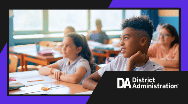 Young students sitting at tables looking ahead. District Administration logo on bottom right.