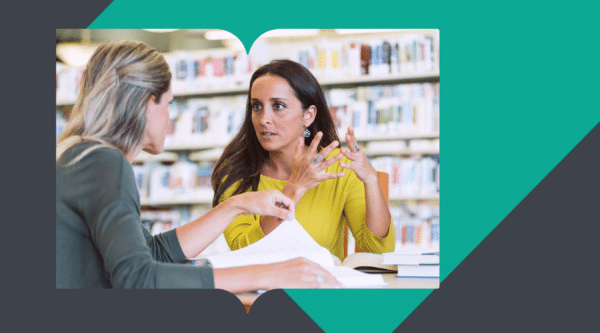 Two women in a library engaged in an intense discussion, with books and notes in front of them, representing communication challenges and strategies in an educational setting.