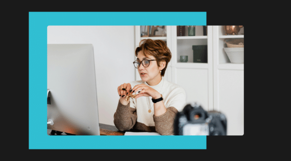 Woman in glasses sitting at desktop with a camera.